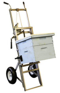 Two-wheeled dolly with hive box held off ground with gripping arms. Hand-operated winch on dolly frame raises and lowers hive box.