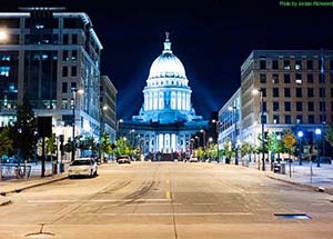 Night photo of city street ending with Wisconsin State Capitol building in distance.