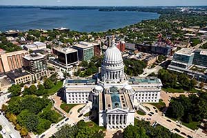 Aerial view of downtown Madison, Wisconsin, with state capitol in foreground and Lake Mendota in background.