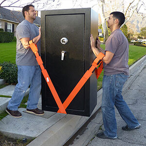 Two men carry large safe using straps looped through their arms and under the safe