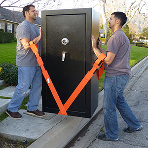 Two men carry large safe using straps looped through their arms and under the safe