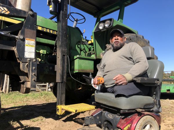 Frank sits in motorized wheelchair next to tractor that has a platform lift to raise him to the cab