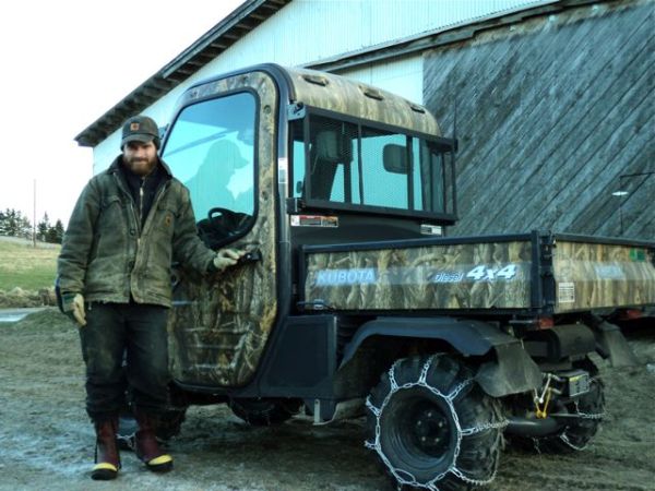 Jessie stands, dressed for cold weather, in front of utility vehicle and barn.