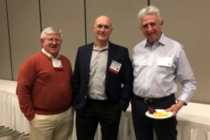 Bill Field, Brad Rein, and Bob Aherin stand in ballroom smiling at camera.