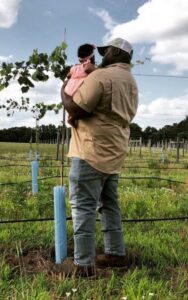 Davon Goodwin holding baby girl while both face a farm fence and field
