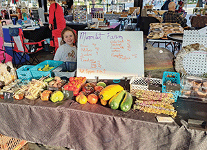 Young girl, smiling at the camera, stands behind table full of vegetables at farmers market