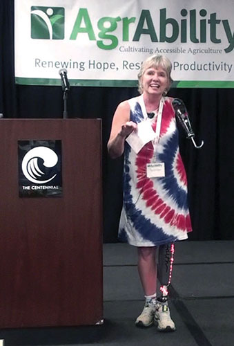 Laurie Hayn speaking on stage next to podium with AgrAbility banner in background