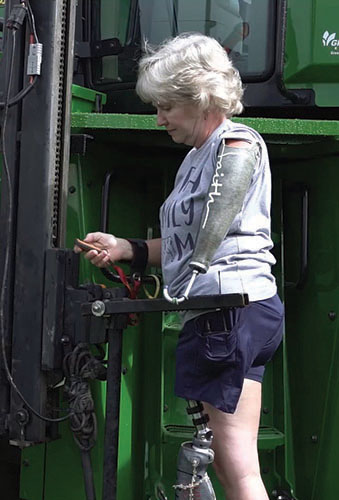 Laurie Hayn, wearing prosthetic left arm and leg, using lift to access tractor cab