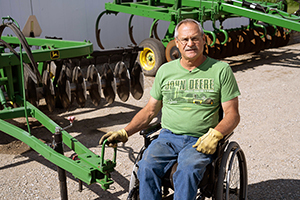 Doug VerHoeven sitting in wheelchair next to farm implements